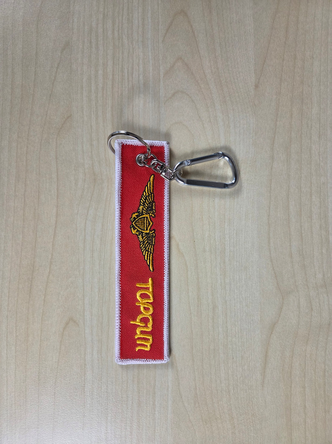Top Gun keychain with red background and yellow text on a wooden surface