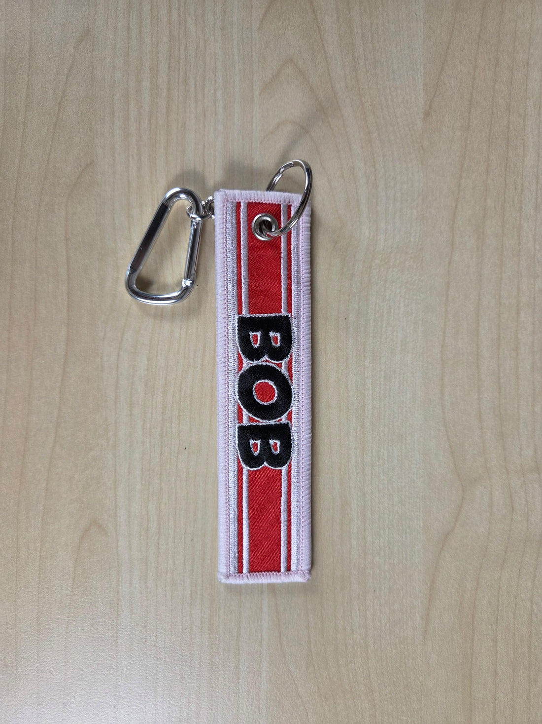 Keychain with 'BOB' on a red and white striped background on a wooden surface
