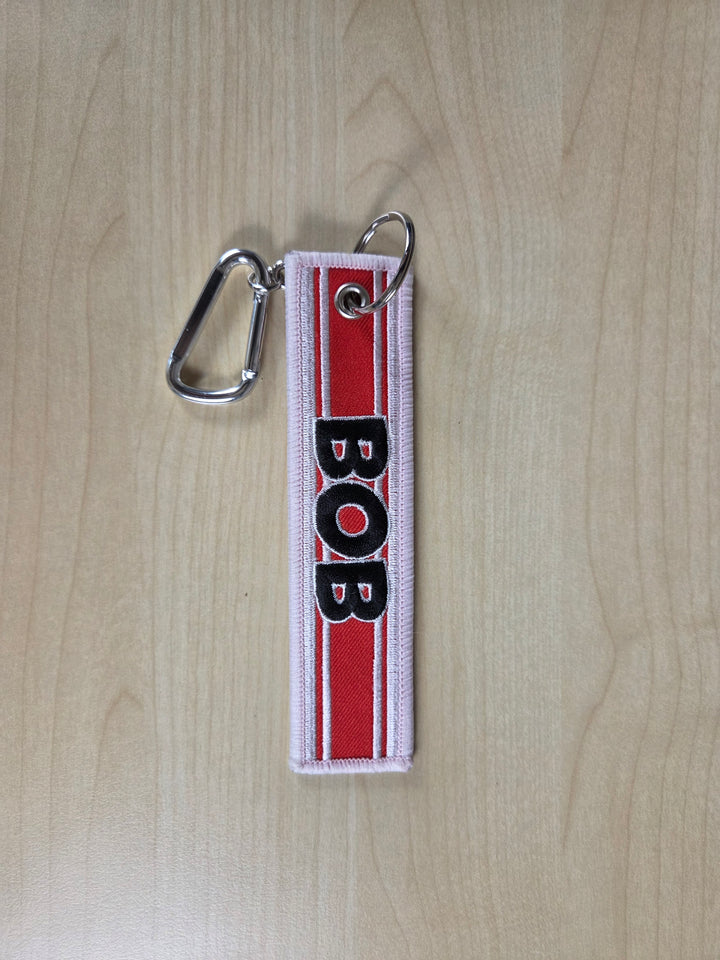 Keychain with 'BOB' on a red and white striped background on a wooden surface