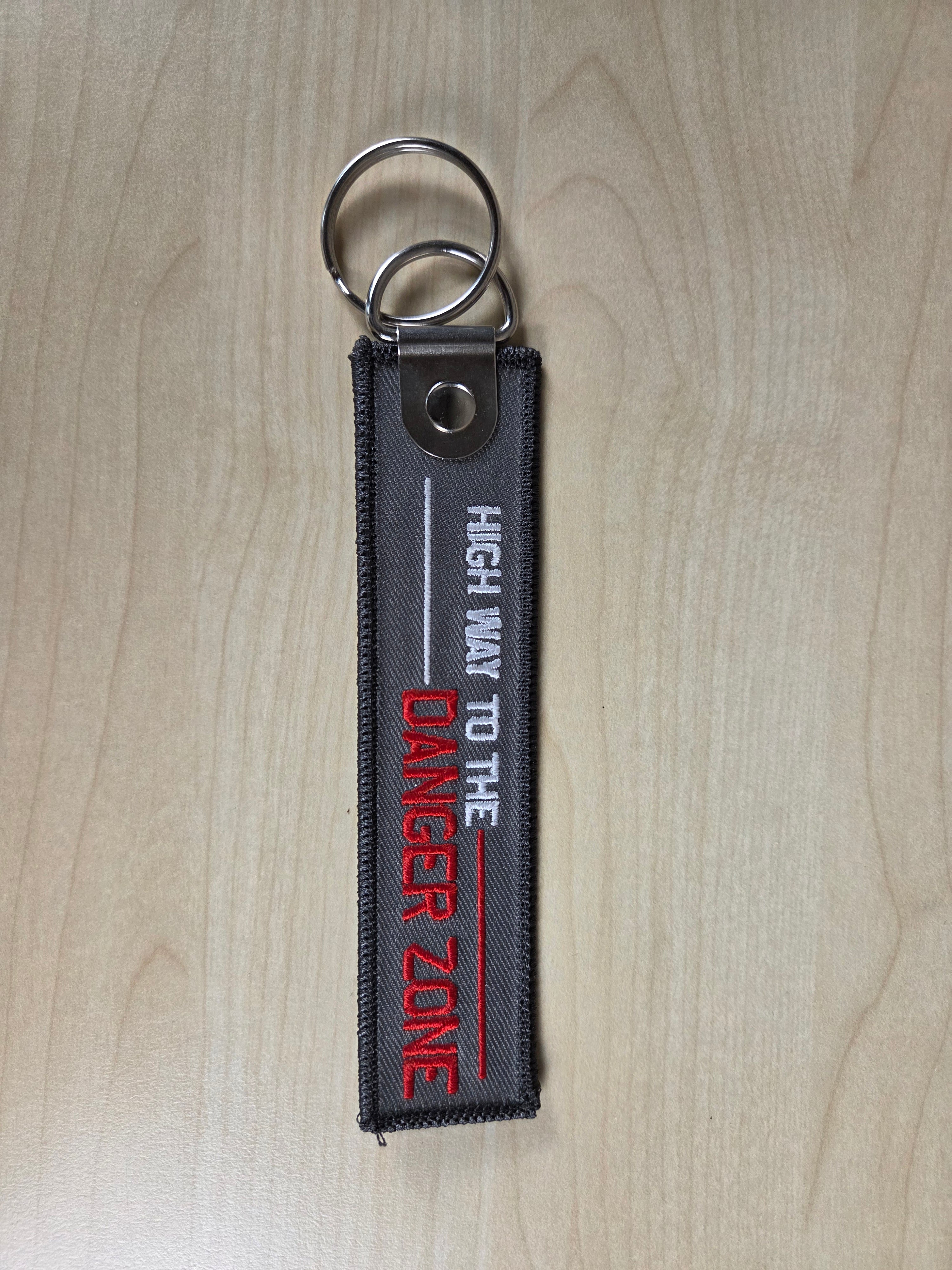 Keychain with 'Highway to the Danger Zone' text on a wooden surface