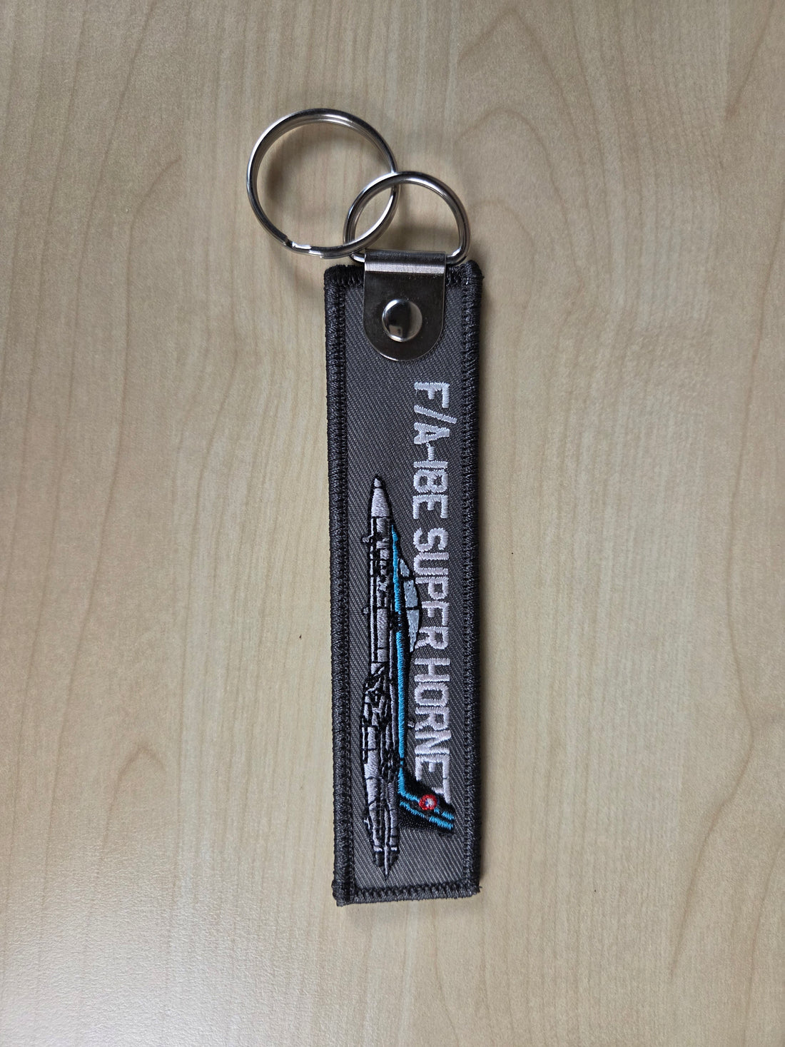 Keychain with F/A-18E Super Hornet design on a wooden surface