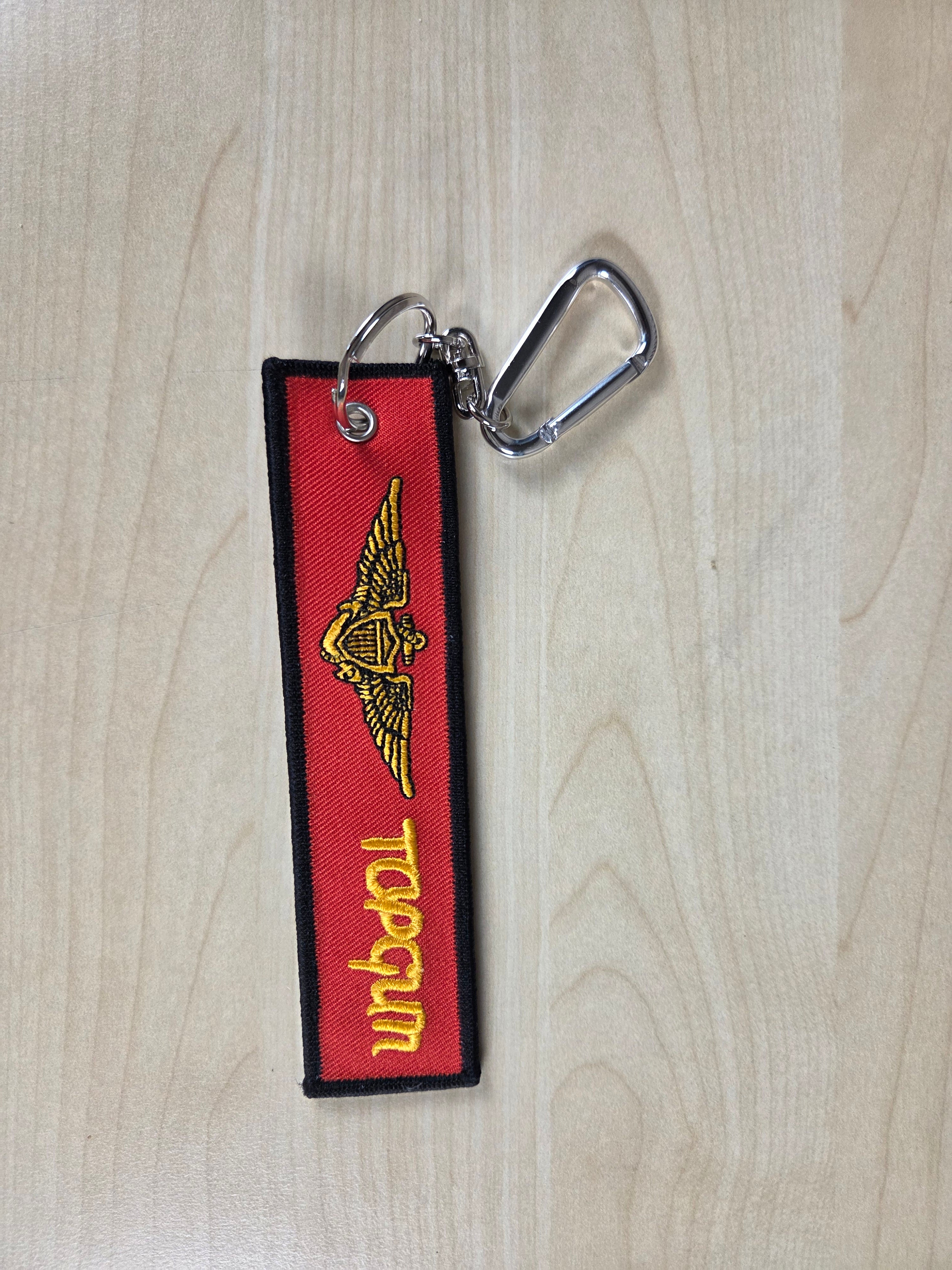 Top Gun keychain with red background and yellow text on a wooden surface