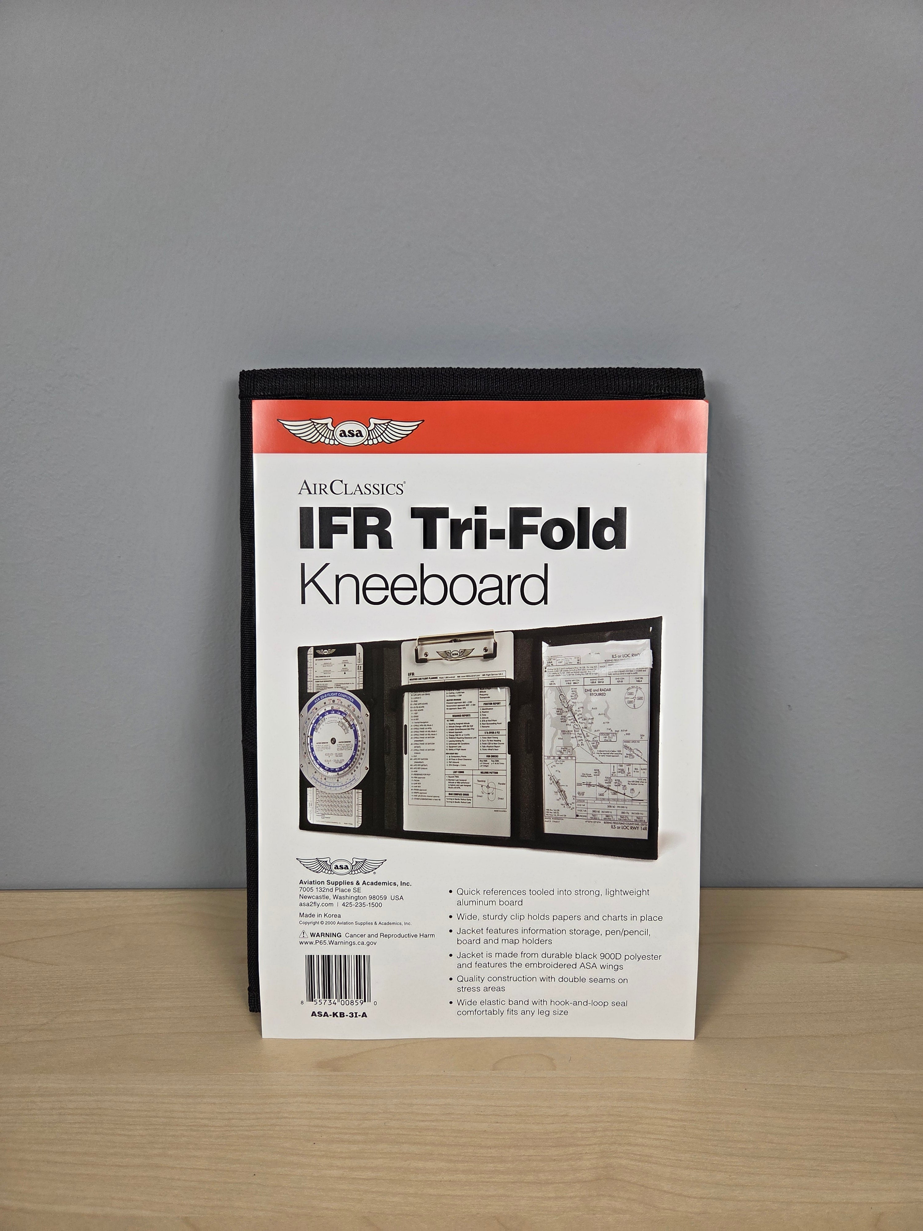 A packaged ASA IFR Tri-Fold Kneeboard document holder standing upright on a light wood surface against a gray wall.