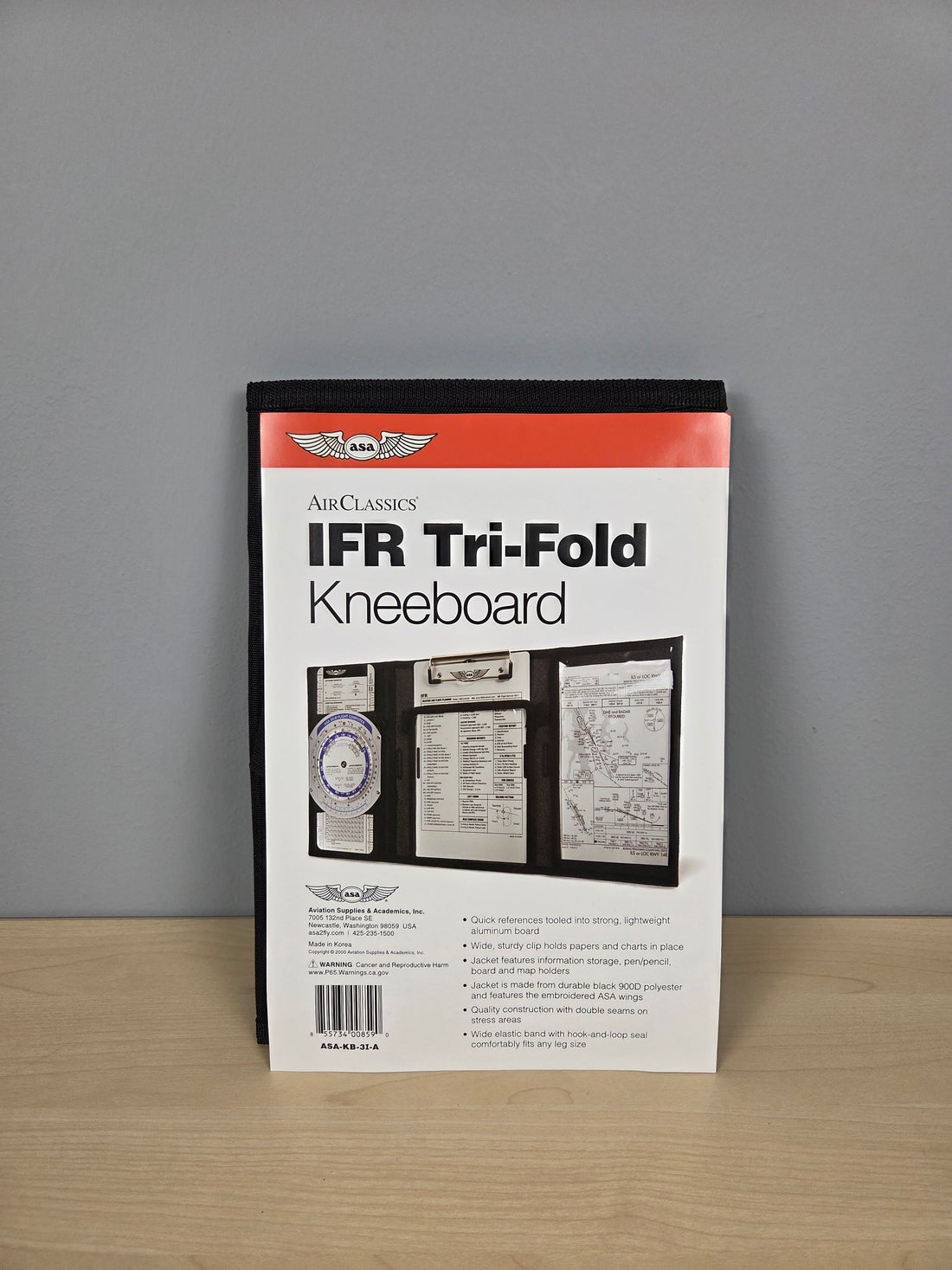 A packaged ASA IFR Tri-Fold Kneeboard document holder standing upright on a light wood surface against a gray wall.