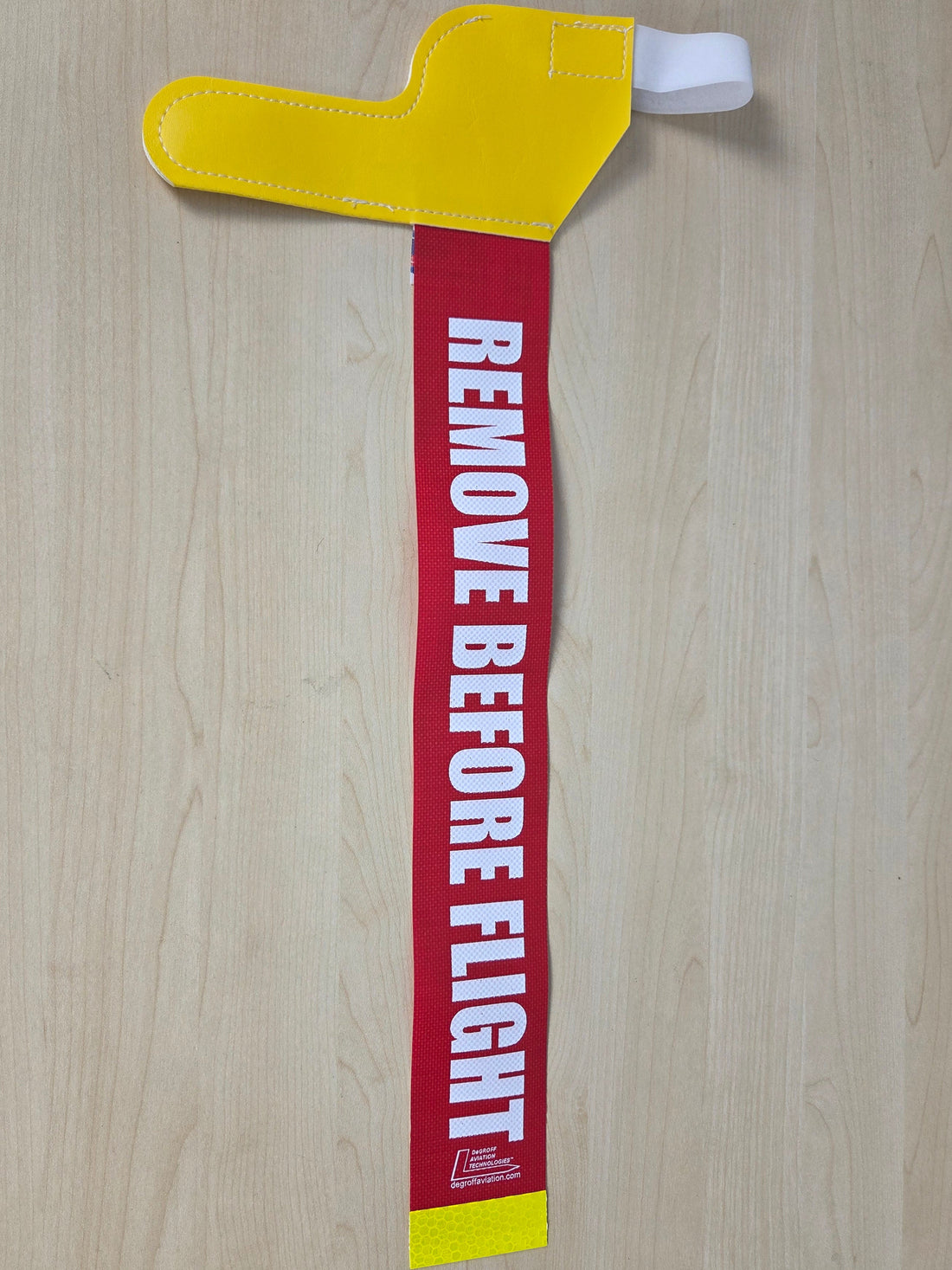 A Yellow pitot tube cover with "remove before flight" tag on top of a wooden grain board 