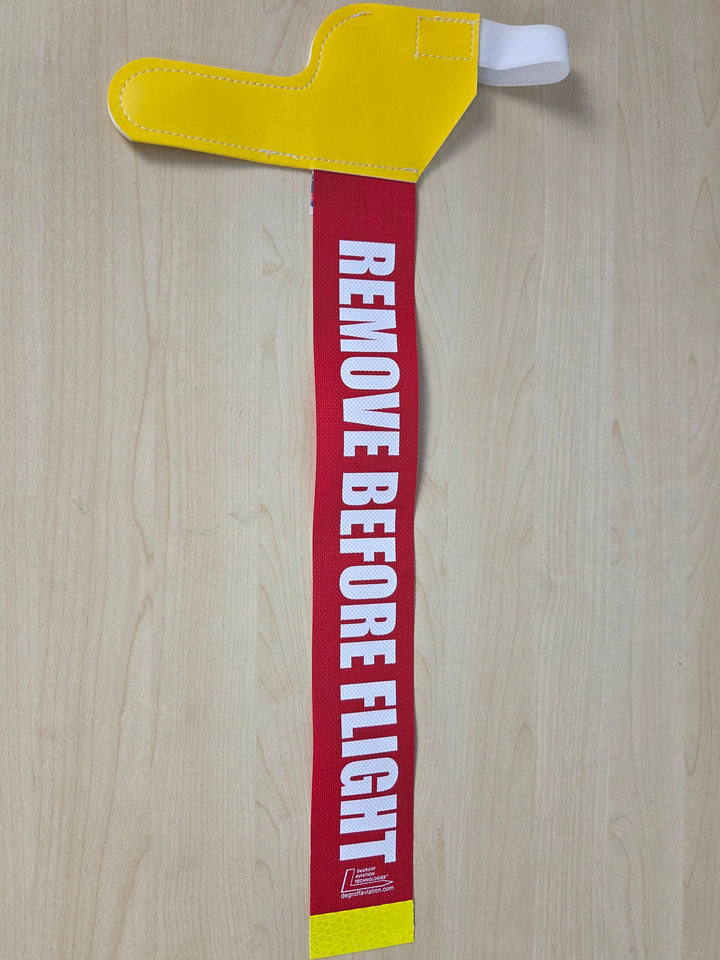 A Yellow pitot tube cover with "remove before flight" tag on top of a wooden grain board 