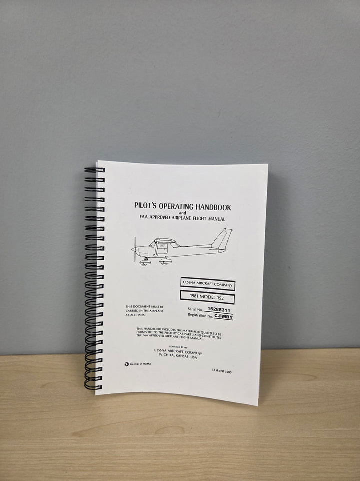 A spiral-bound Pilot's Operating Handbook for a Cessna 172 aircraft, displayed standing upright on a light wood surface against a neutral gray wall.