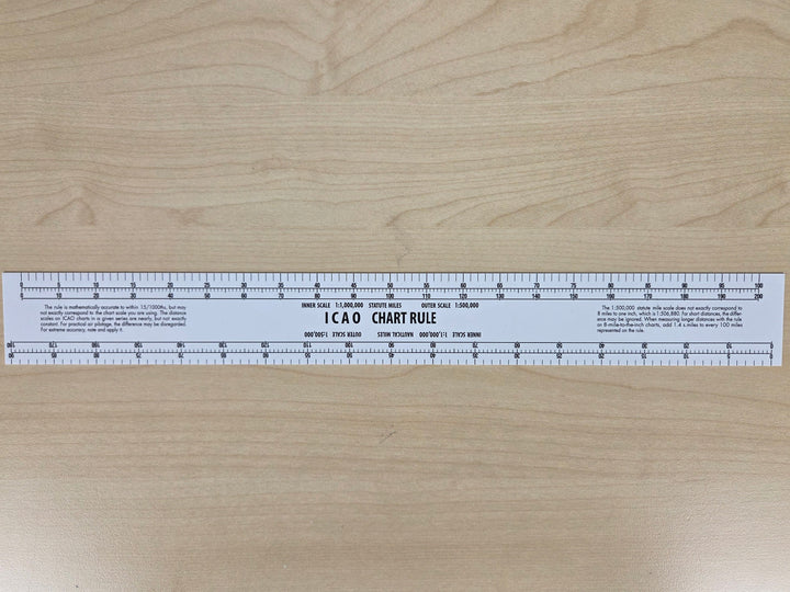 A white plastic 12 x 6 inch aviation chart ruler with printed measurement markings, shown vertically on a light wood grain surface.