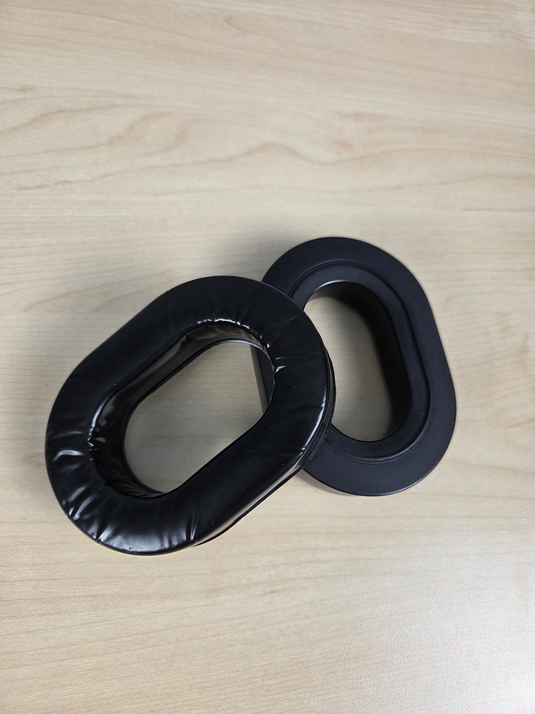Two black padded replacement headband aviation headset ear cushions resting on a light wood grain surface.