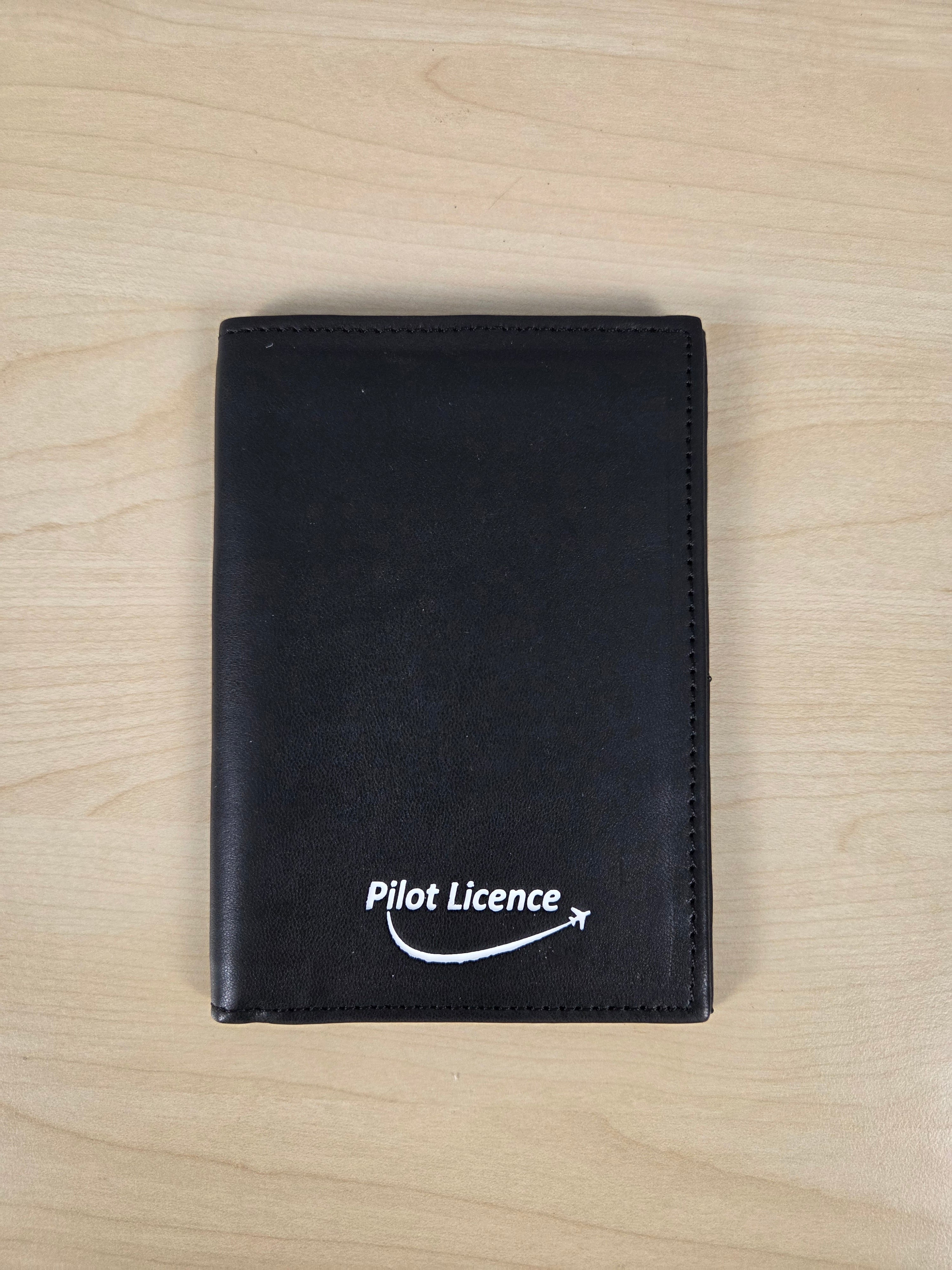 A black leather wallet with a white 'Pilot Licence' logo printed on the front, displayed flat on a light wood grain surface.