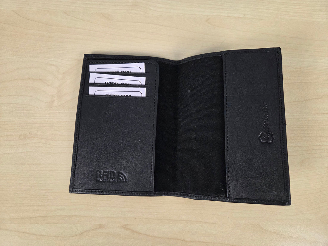 A black leather bifold wallet shown open on a light wood grain surface, displaying its interior card slots, a black velvet-like center pocket, and an embossed logo on the left panel.
