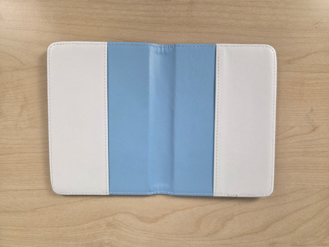 A tablet sleeve with a vertical color-blocked design of white, light blue, and white, shown open on a light wood grain surface.