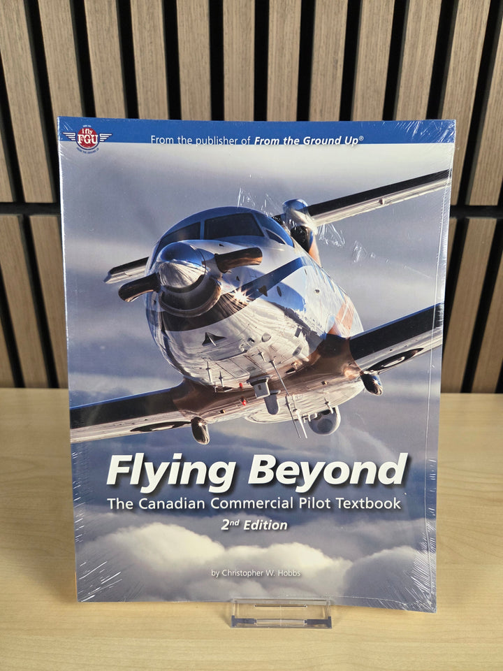 Book titled 'Flying Beyond: The Canadian Commercial Pilot Textbook' on a wooden surface with a blurred background.