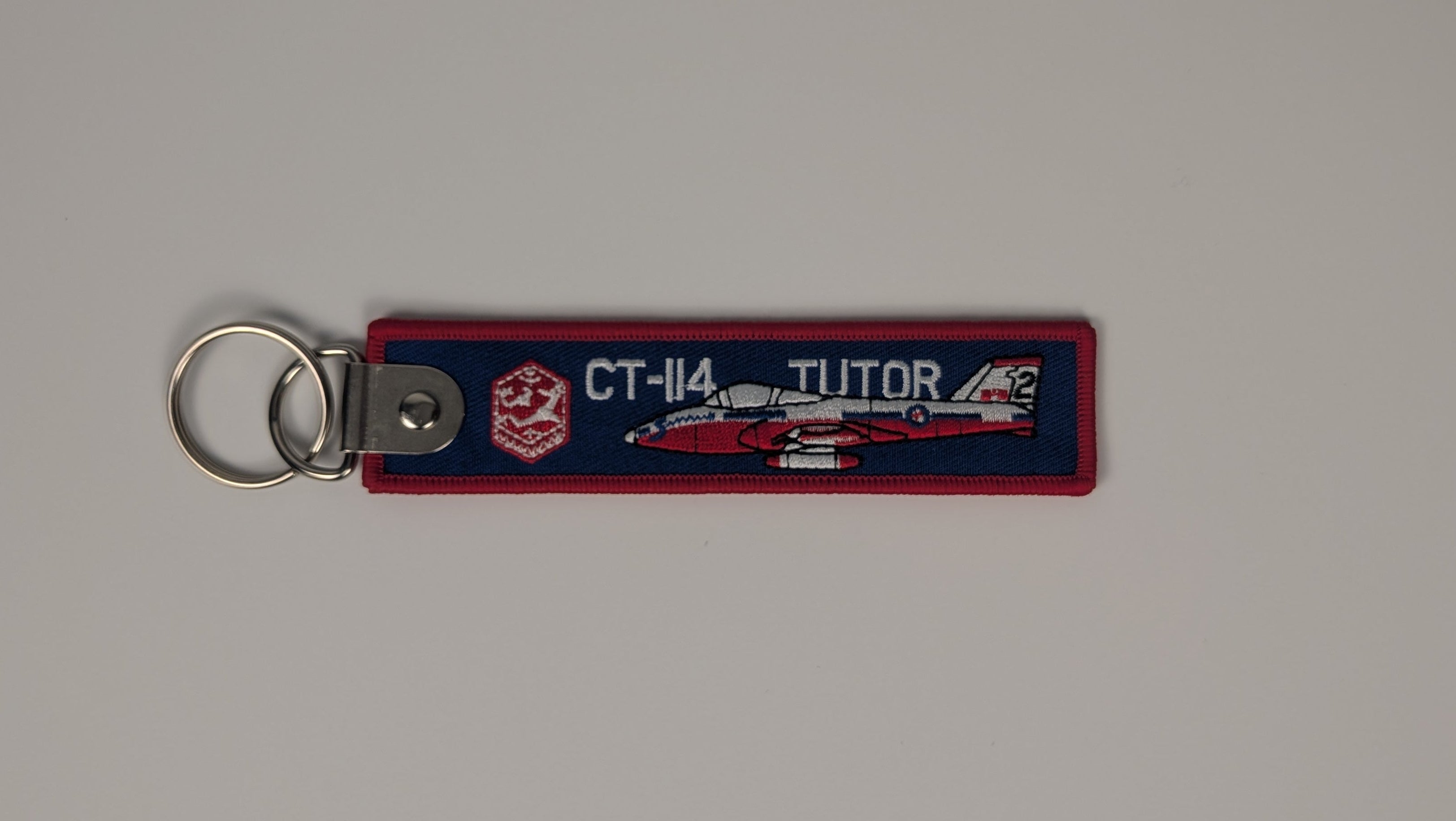 A rectangular fabric keychain featuring a red and navy blue fire department design with a white jet graphic and the text 'CT-14 JETTOR', attached to a silver metal split ring on a neutral gray background.