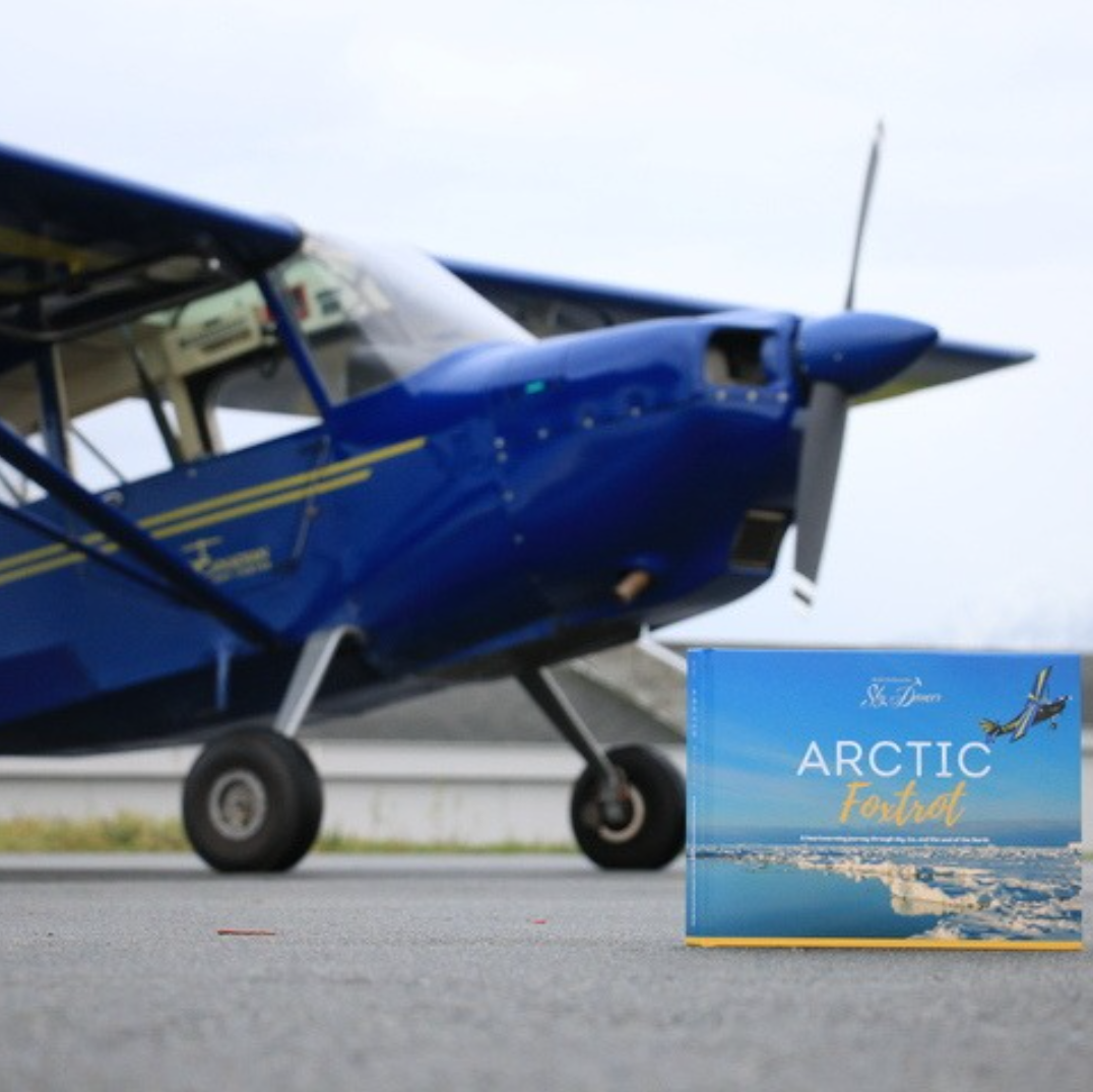 Blue airplane on a runway with a book titled 'Arctic Foxtrot' in the foreground